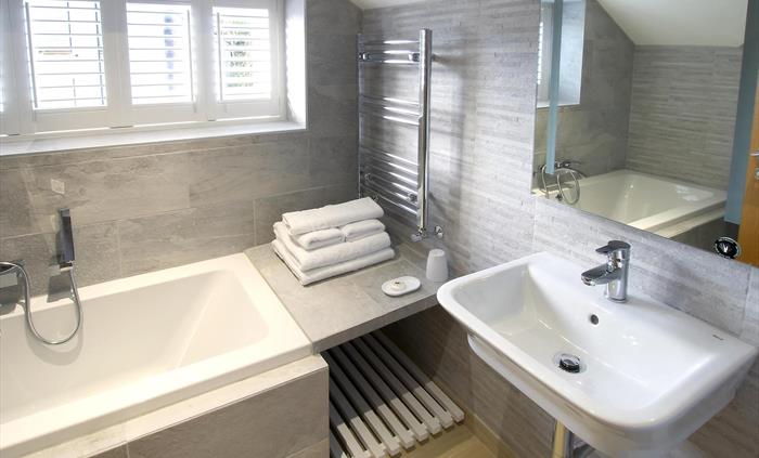 Elegant bathroom with a deep bathtub, heated towel rail, and modern basin set against stone-effect tiles.